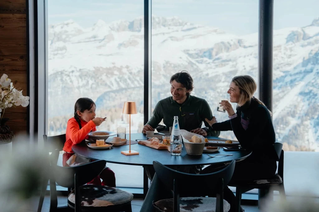 A family enjoys a meal at a table with a snowy mountain view.