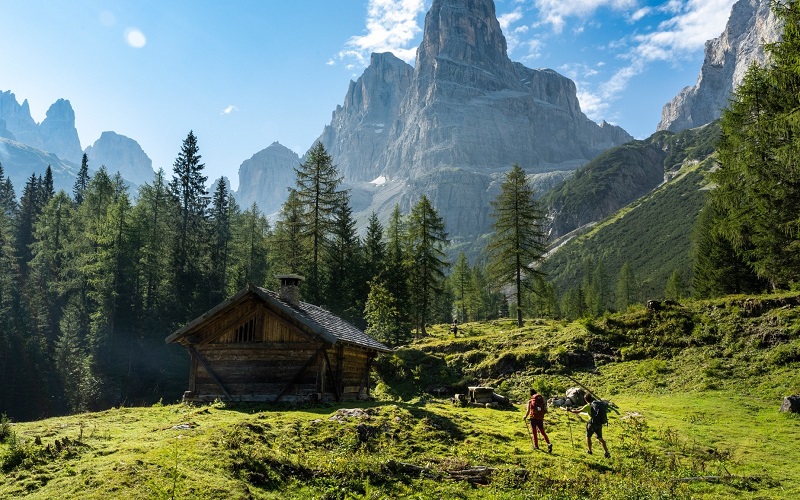 A small wooden cabin in a mountainous landscape with hikers nearby.