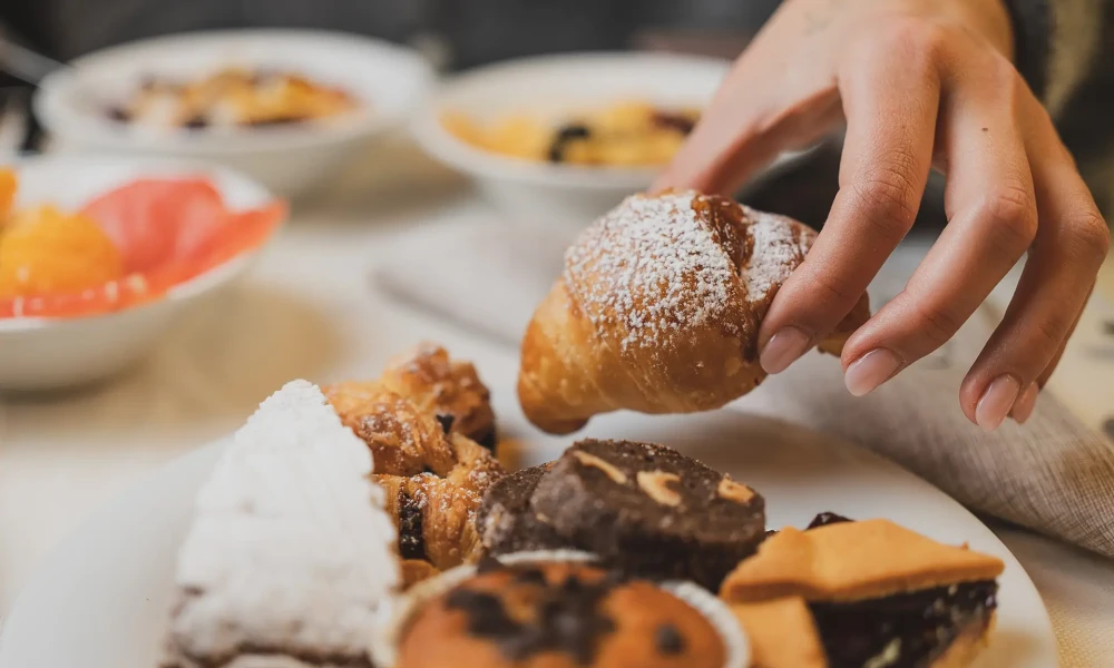 Mano che prende un cornetto da un piatto di dolci.