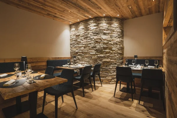 Interno di un elegante ristorante con arredi in legno e parete in pietra.