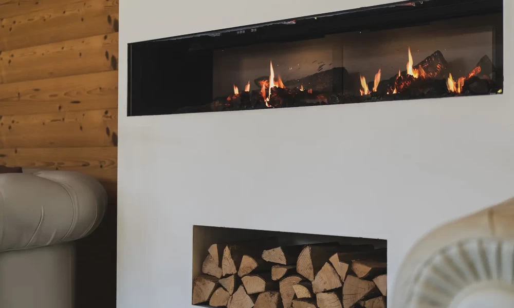 A modern indoor fireplace with stacked firewood below.