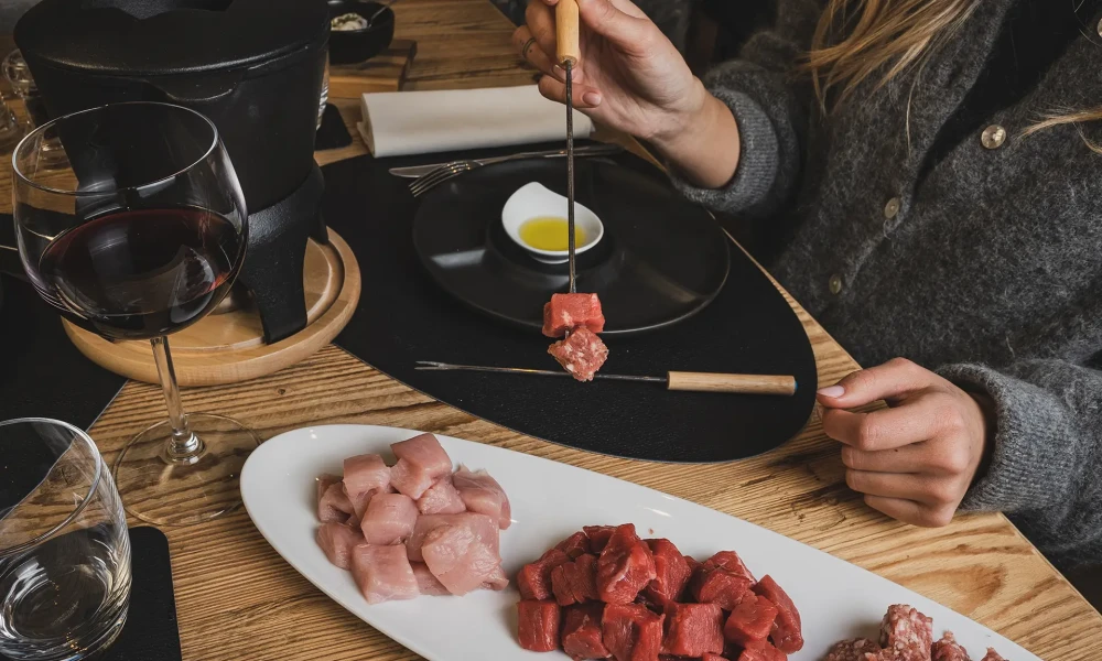 Persona che prepara una bourguignonne con carne cruda e un bicchiere di vino rosso su un tavolo di legno.