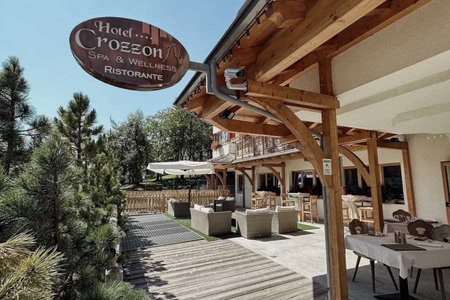 Outdoor seating area of Hotel Crozzon with wooden architecture under a clear blue sky.