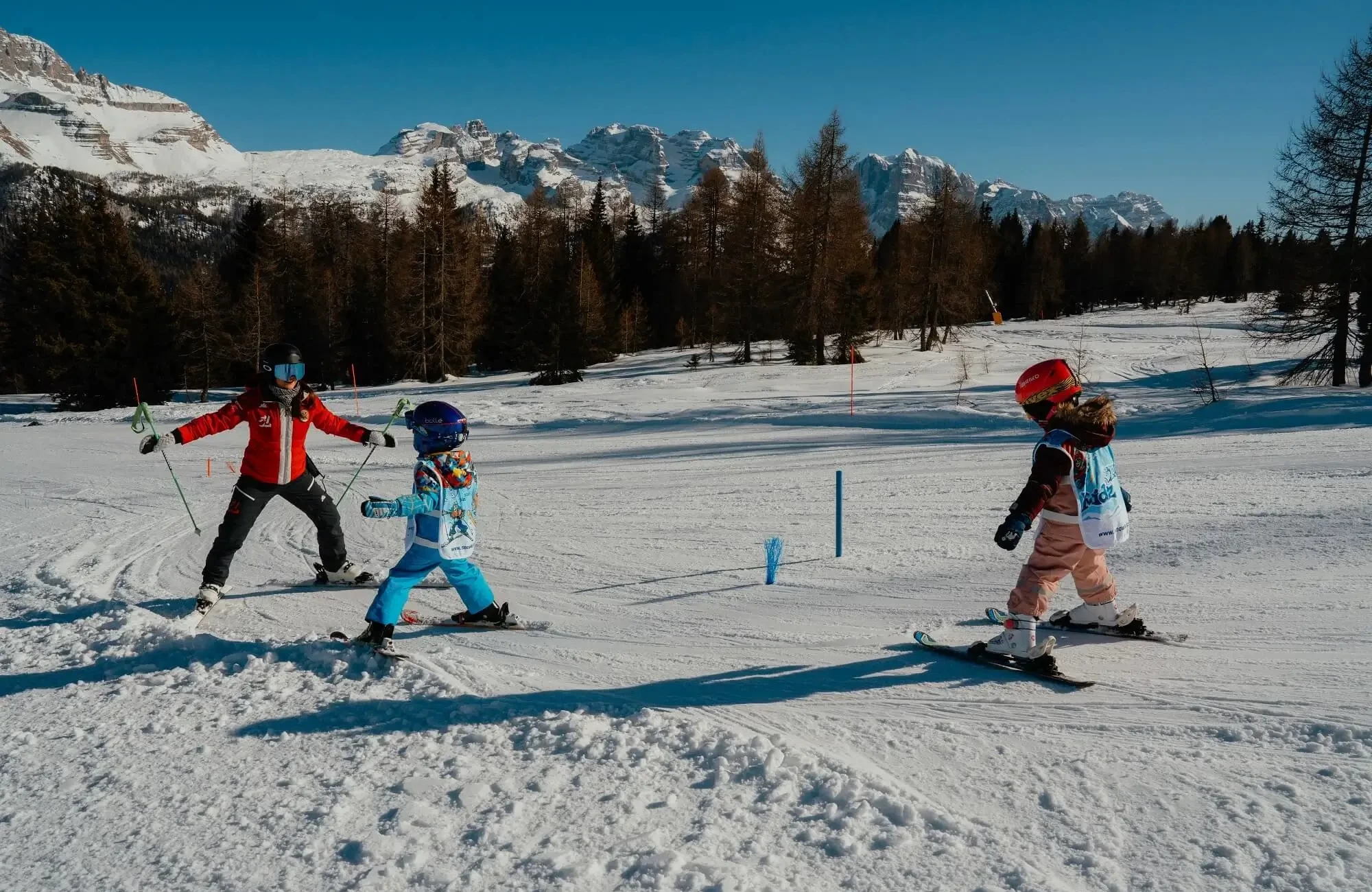 An instructor teaches two young children how to ski on a snowy mountain slope.