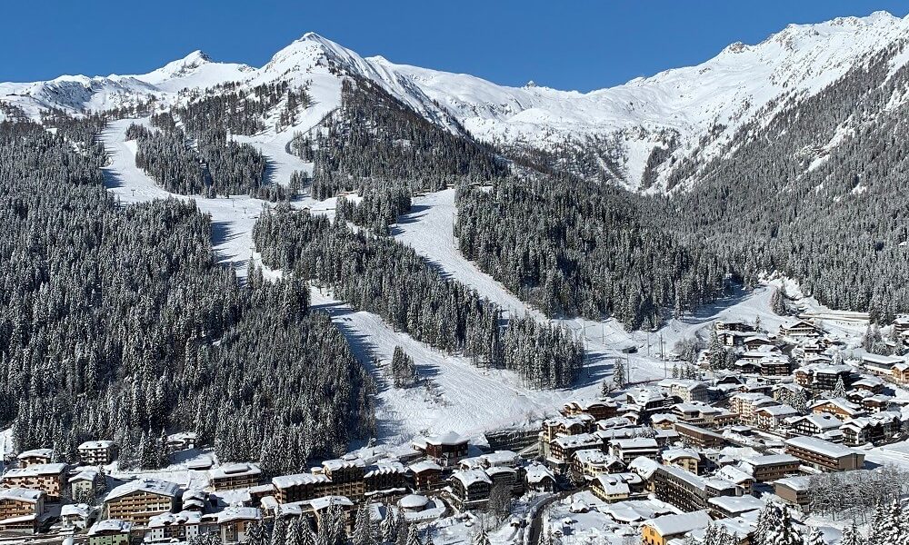 Vista panoramica di una stazione sciistica innevata tra le montagne sotto un cielo terso.