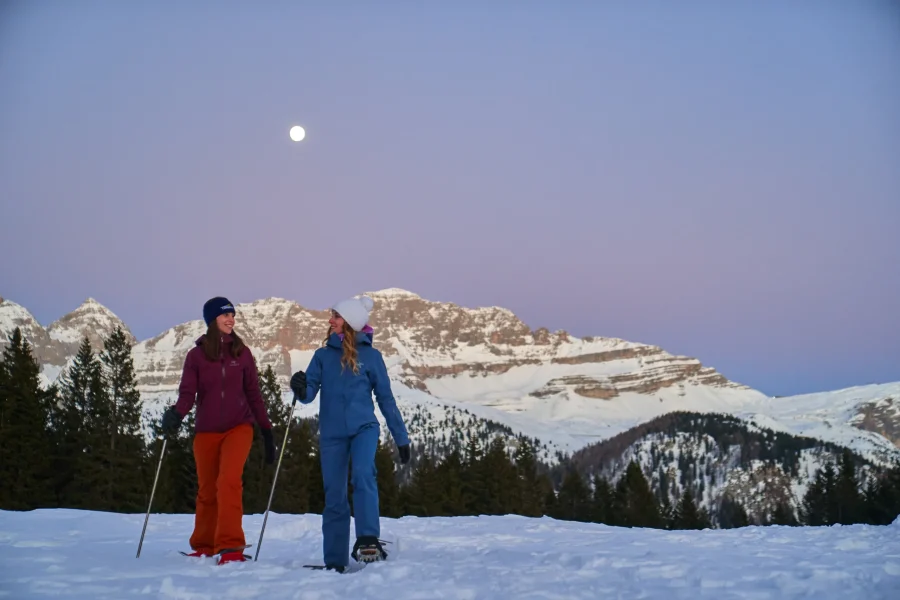 Due amiche con le ciaspole sotto la luna piena, con le Dolomiti rosate al tramonto