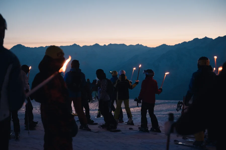 Sciatori con le fiaccole sulla neve al tramonto durante il Sunset Ski