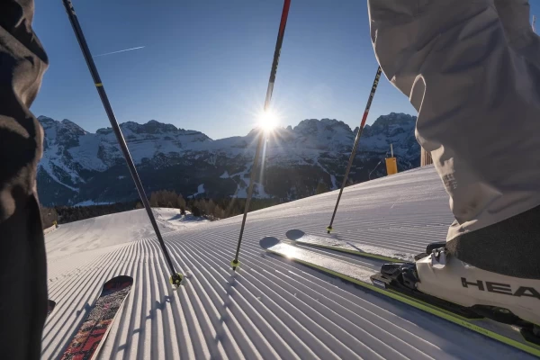 Skier on a snowy slope with mountains and a setting sun in the background.
