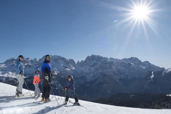 A group of skiers on a snowy mountain with a sunny sky and mountains in the background.