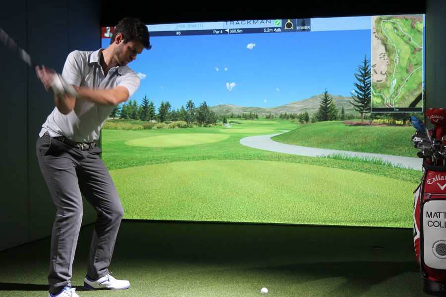 A person swinging a golf club in front of a golf simulator screen.