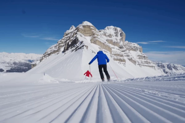A skier and a child on a snowy mountain slope under a clear blue sky.