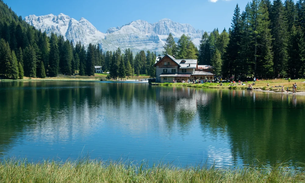A serene mountain lake with a cabin and trees reflected in the water.
