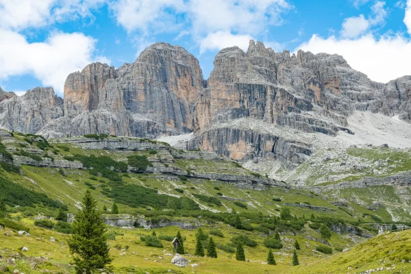 A scenic view of rugged mountains towering over a green valley with scattered trees and a bright blue sky.