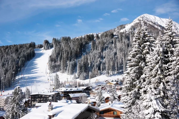 Paesaggio alpino innevato con piste da sci e chalet di montagna.
