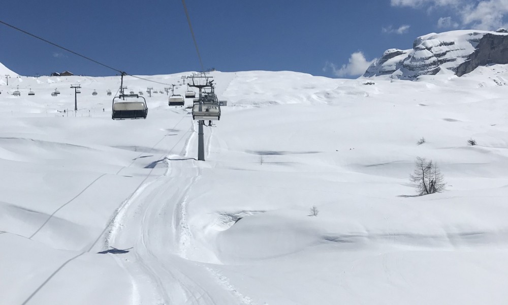 A ski lift ascends a snowy mountain under a clear blue sky.